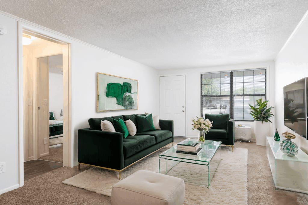 A furnished apartment living room with a green velvet sofa and glass coffee table at Palm Harbor Villas
