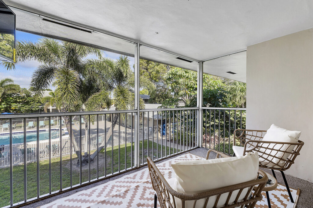 A screened balcony with woven armchairs overlooking the pool and palms at Waterford Bay Apartments